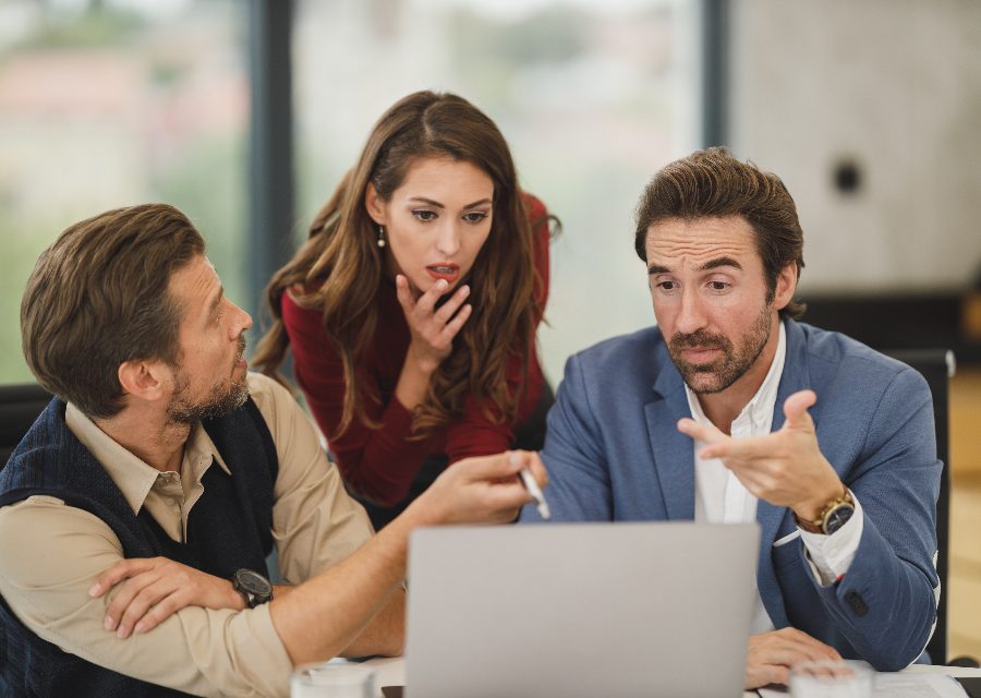 Three colleagues gathered around a laptop, mid-conversation.